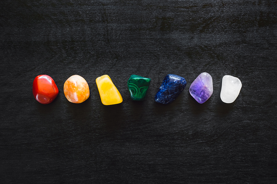 Sept cristaux polis alignés sur une surface noire, représentant les couleurs et énergies des chakras.