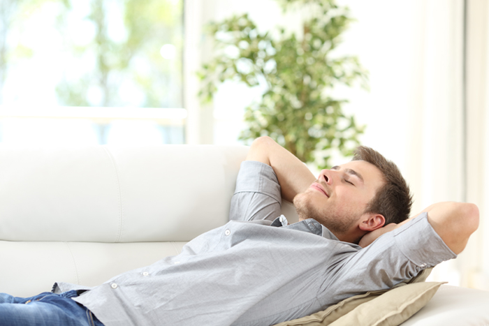 Homme détendu, allongé sur un canapé, les mains derrière la tête, profitant d'un moment de relaxation profonde.