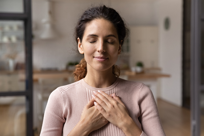 Femme les yeux fermés, les mains posées sur le cœur, exprimant un moment de reconnexion intérieure et d'apaisement émotionnel.