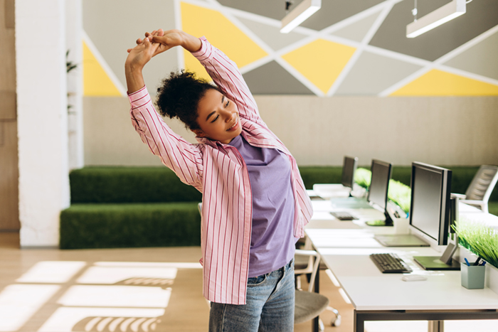 Jeune femme s'étirant dans un espace de travail lumineux, les bras tendus au-dessus de la tête.