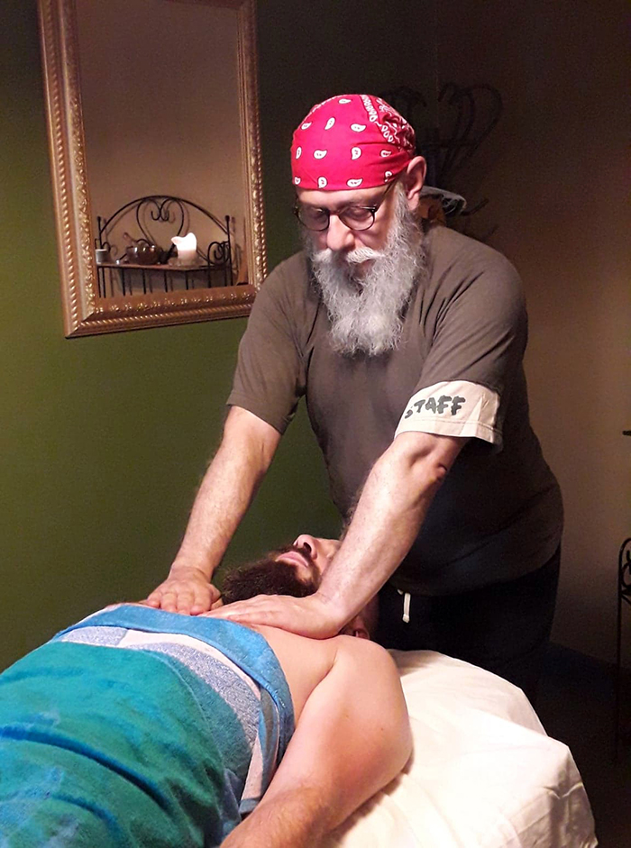Juan Carlos, praticien de massage californien chez EMPAB, effectue un massage sur un client allongé, dans un cadre chaleureux et apaisant.